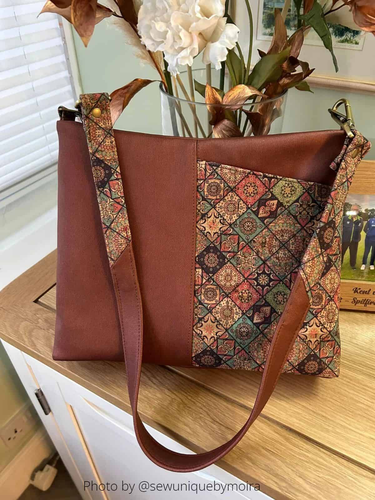 an elegant handmade handbag in brown faux leather and printed cork, placed on an oak tabletop