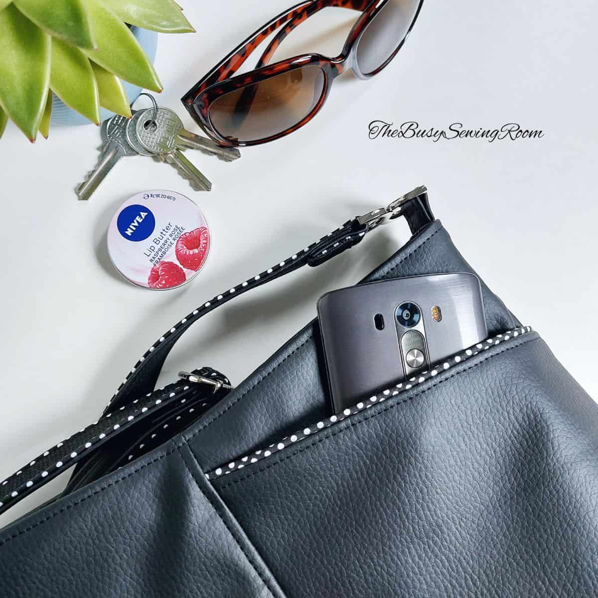 a handmade bag with a front exterior pocket, sewn with with black faux leather, next to sunglasses, keys, and a lip balm