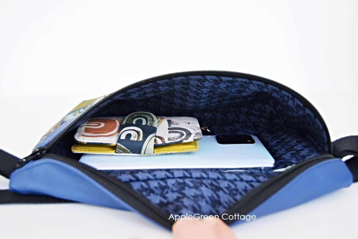 an open blue faux leather hip bag with a view into the interior, carrying a small wallet and a cell phone, with plenty of space left
