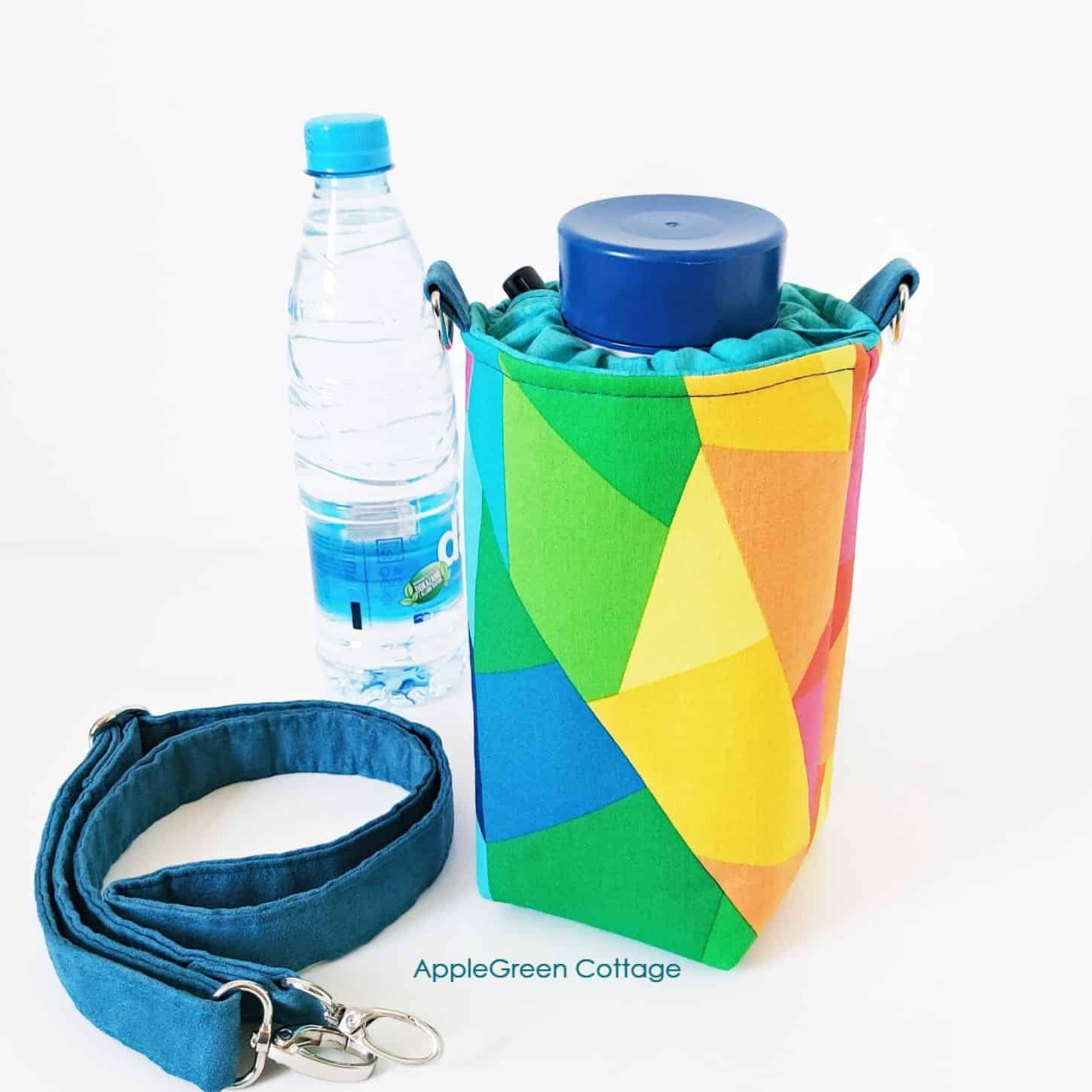 a finished water bottle holder in bright cotton print with top closure and a crossbody strap, with a water bottle in the background
