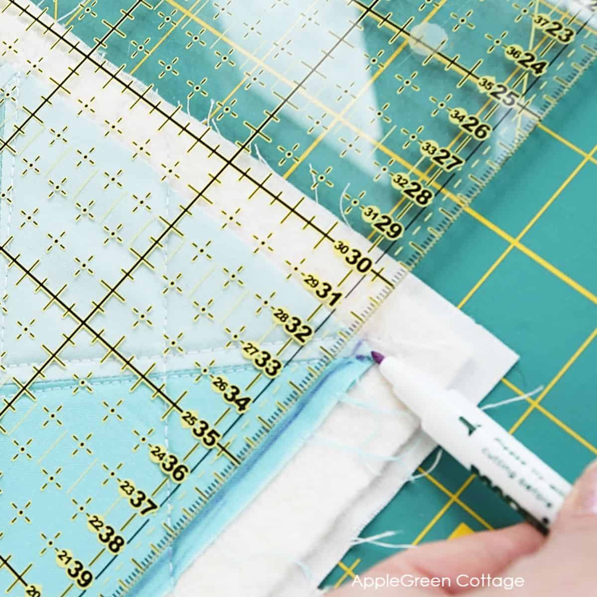 a hand holding a fabric marker and marking a quilted and pieced quilt to square it up