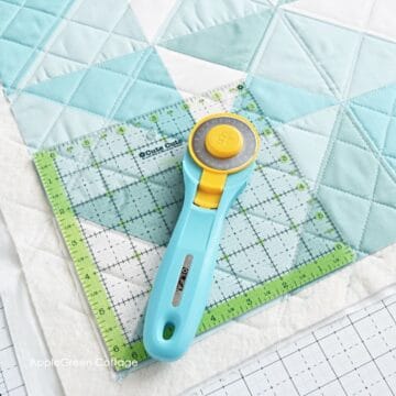 aqua rotary cutter on a square quilting ruler placed on a sandwiched quilt ready to be squared up