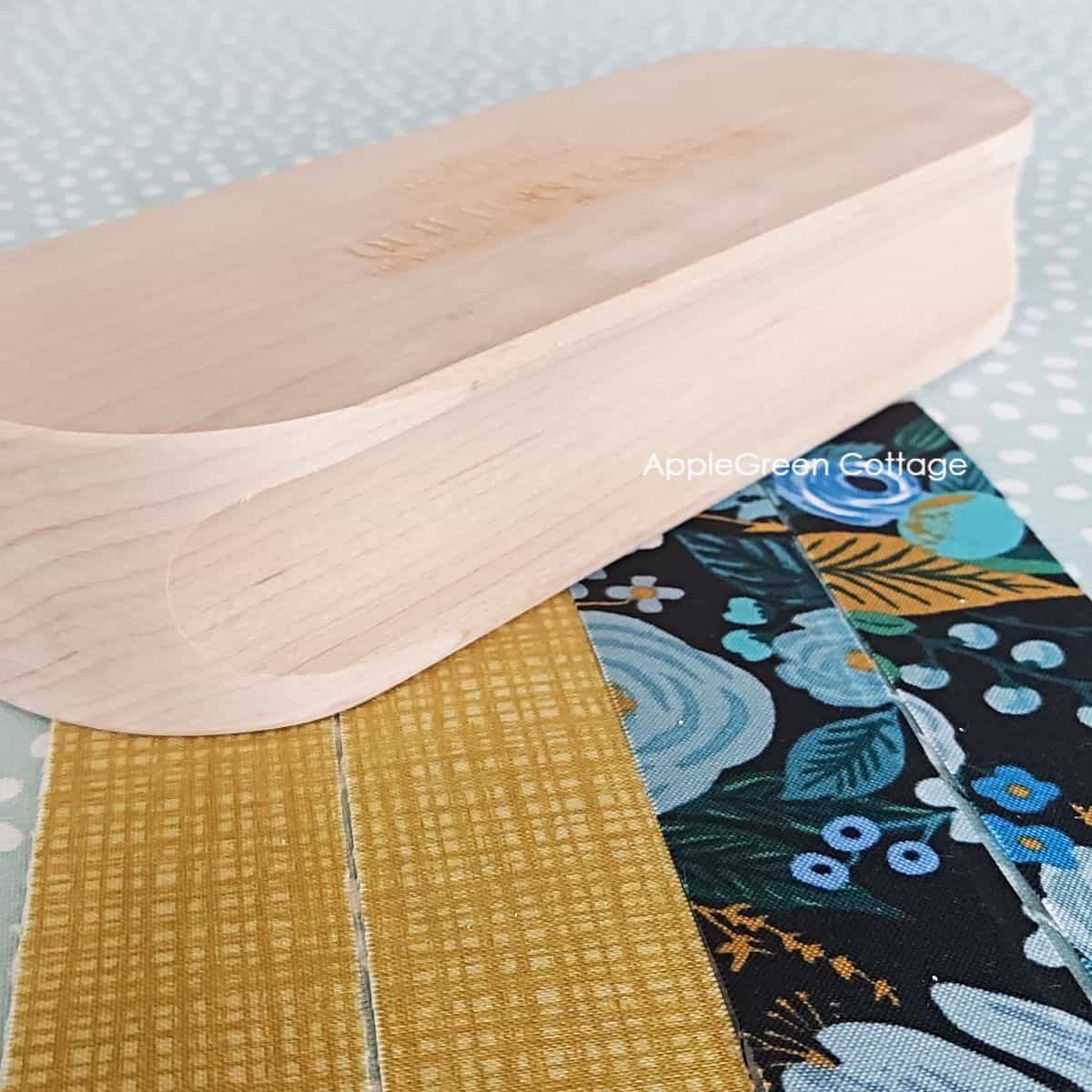 a wooden quilters clapper placed on four pieces of quilting cotton to flatten seam allowance
