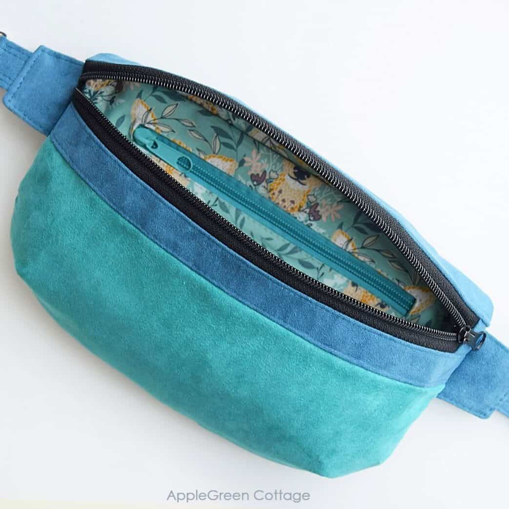 a finished hipbag in blue and teal faux suede with the top zipper open and two darts that give this bag structure and volume