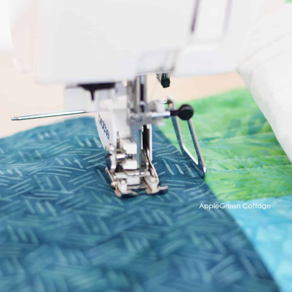 a sewing machine with a walking foot sewing through a quilt sandwich in aqua and green prints