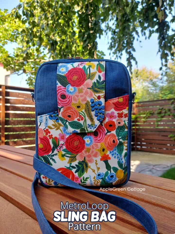 a finished handmade sling bag in denim blue and Rifle Paper floral print set on a wooden tble in a beautiful, summer backyard of an urban home