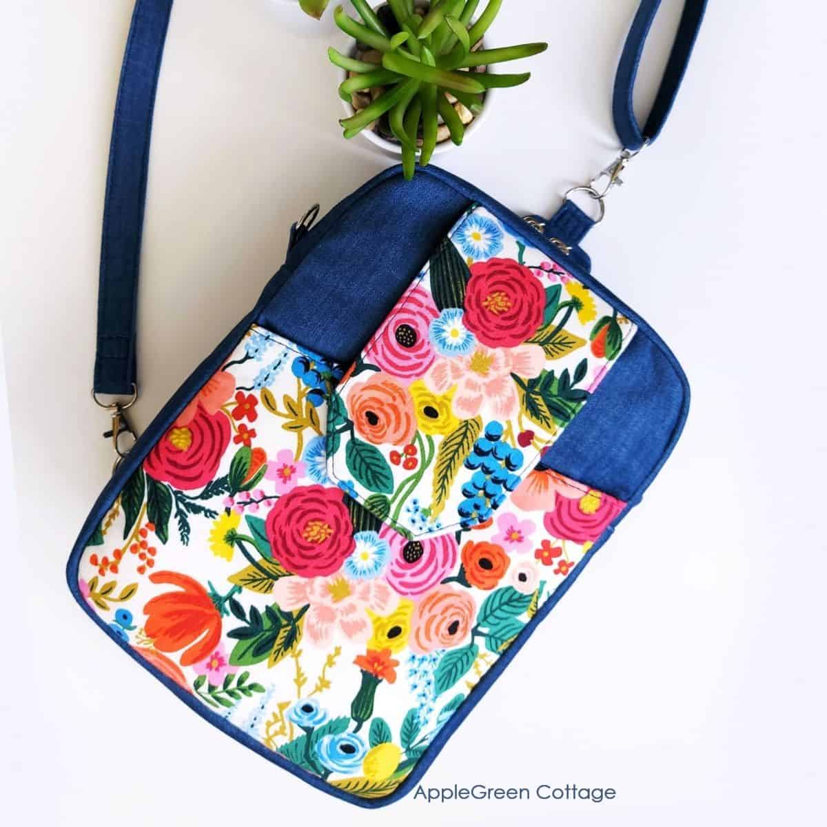 a finished handmade sling bag in deep blue and Rifle Paper floral print, with a flap pocket in the front and a crossbody strap attached