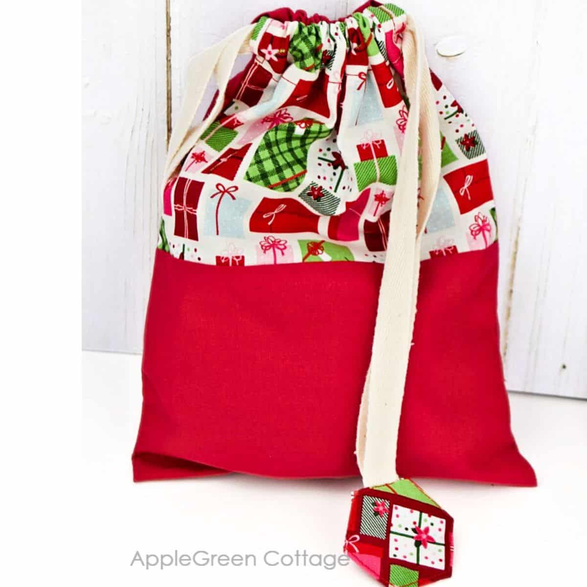 diy gift bag a finalized, color-blocked fabric gift bag propmted against a wall, filled with gifts and tied off using cute drawstring stoppers