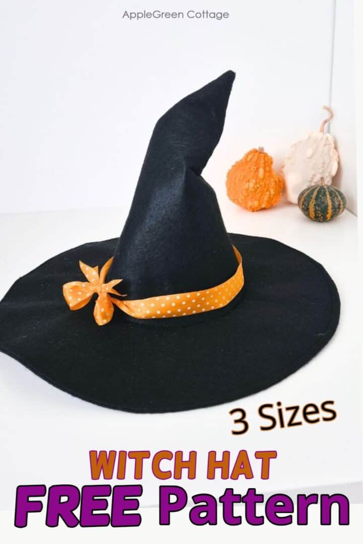 a black witch hat sewn from black felt with a wide brim, an orange polka dot ribbon and a crooked hat top, placed next to three pumpkins