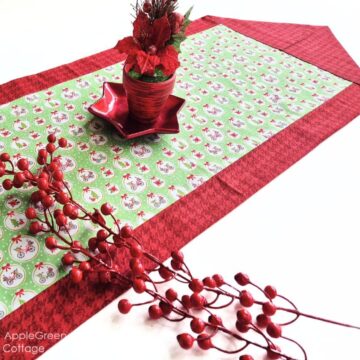 a finished fabric table runner sewn with two fabric pieces in Christmas prints, with a red glossy star-shaped plate on it and 2 stems of holly red berries