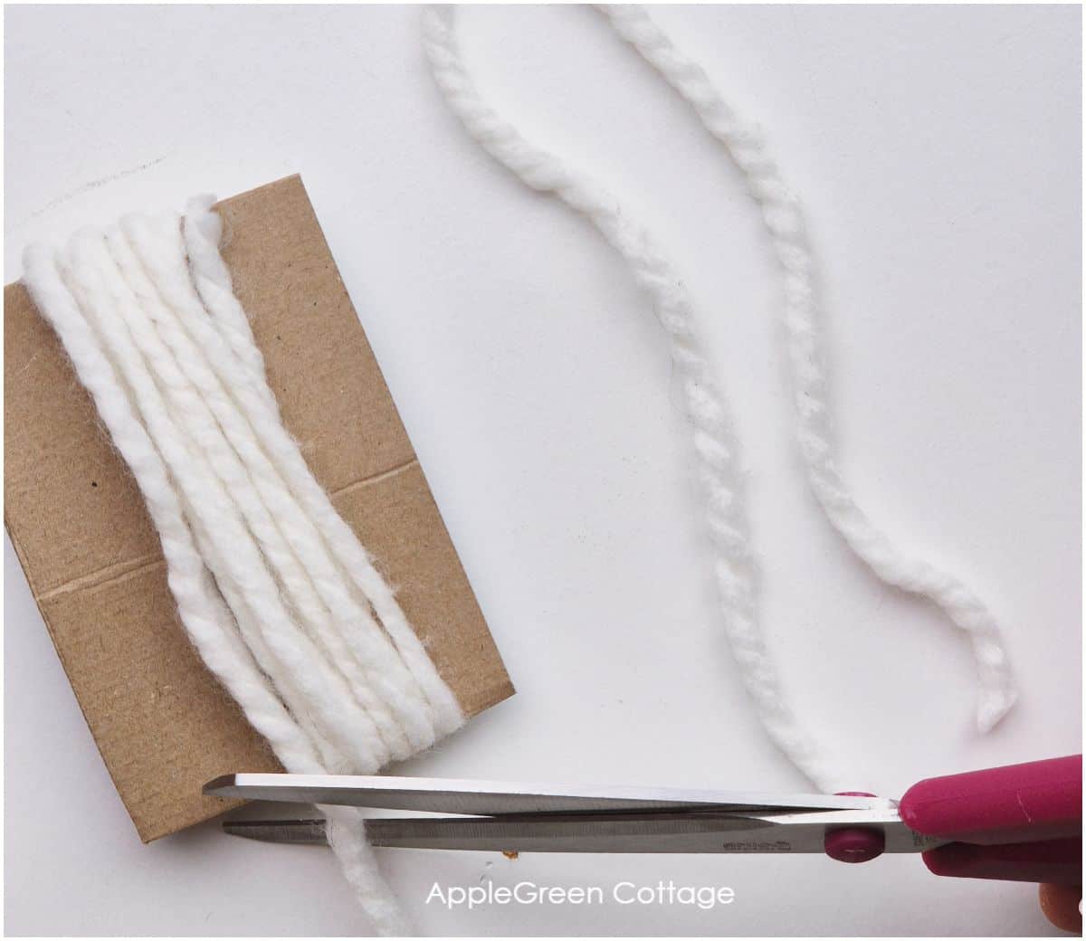 thick chunky off-white yarn wrapped around a piece of cardboard, with scissors cutting it