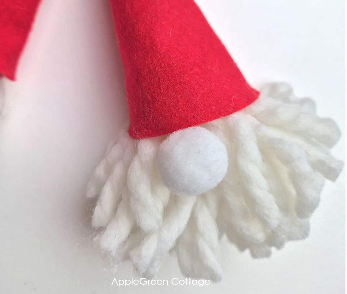 a finished pompom gnome head with a red felt hat and a white pom pom nose