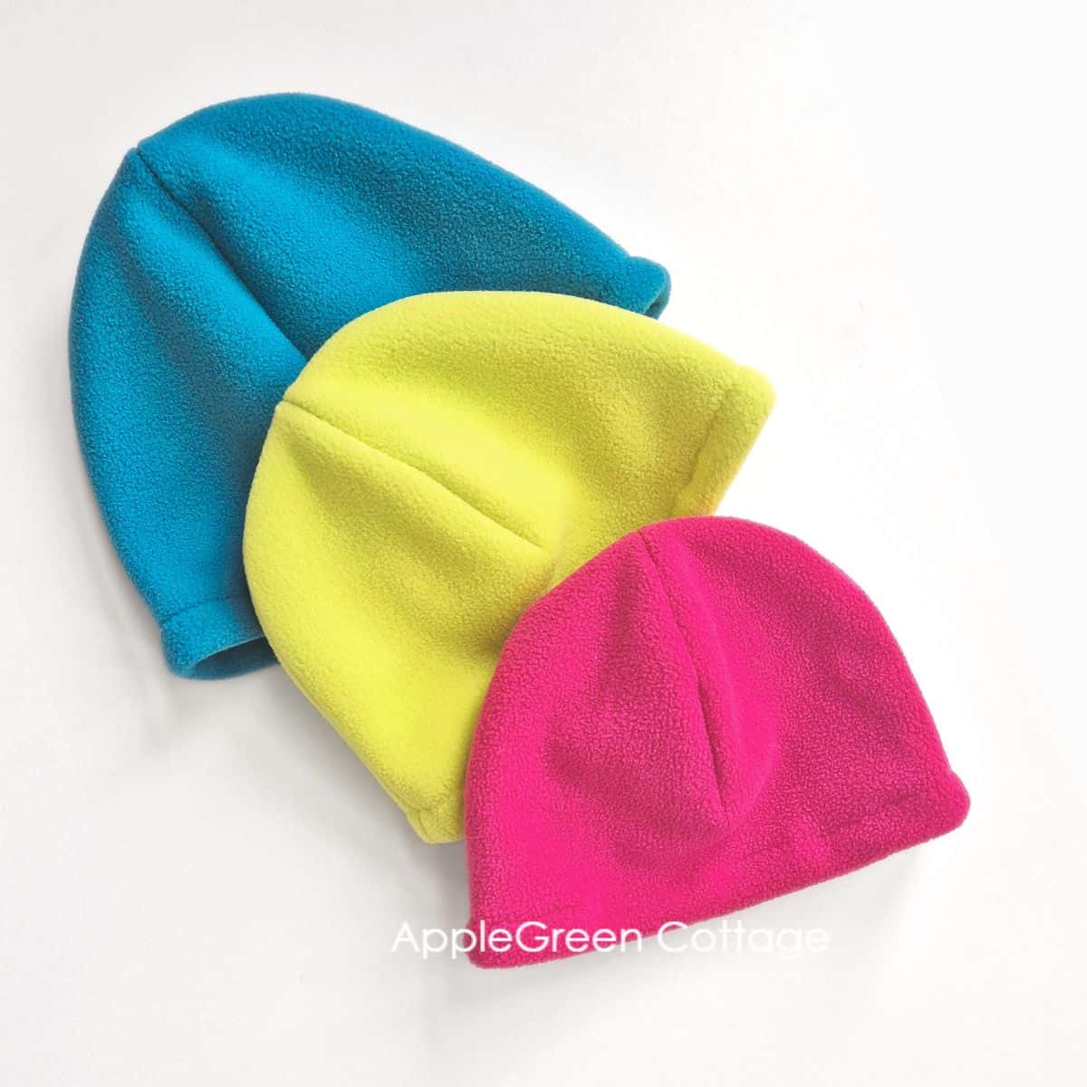 three finished fleece beanies in teal, hot pink and neon colors