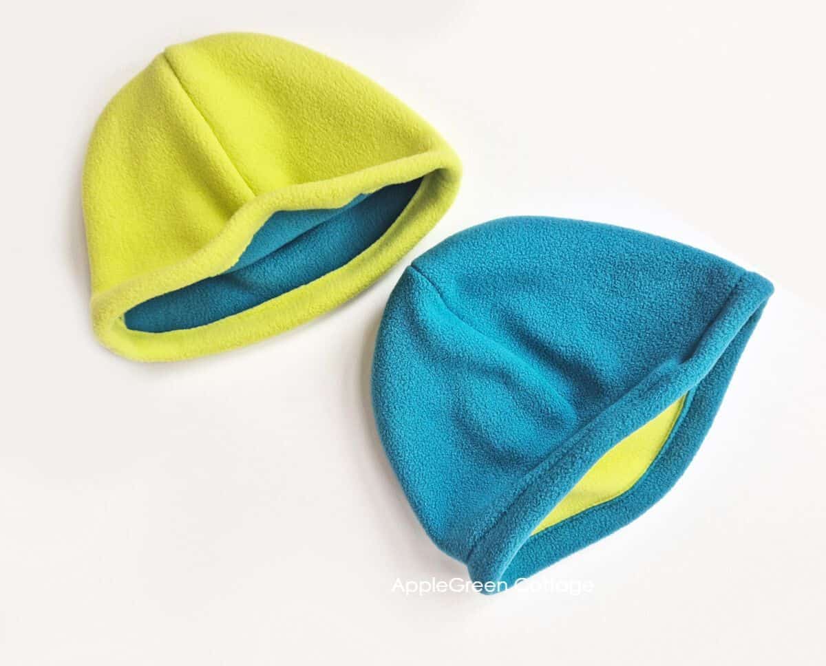 two finished fleece hats sewn with double-sided fleece in teal and neon colors