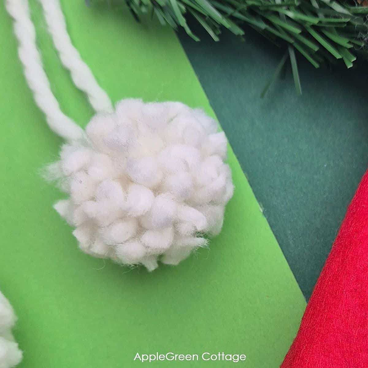 a finished tiny pompom with white yarn on a green background