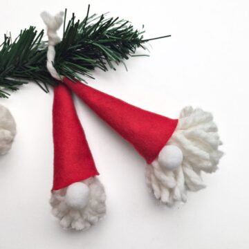two handmande gnomes made from a diy pompom and a red cap using a free gnome hat pattern