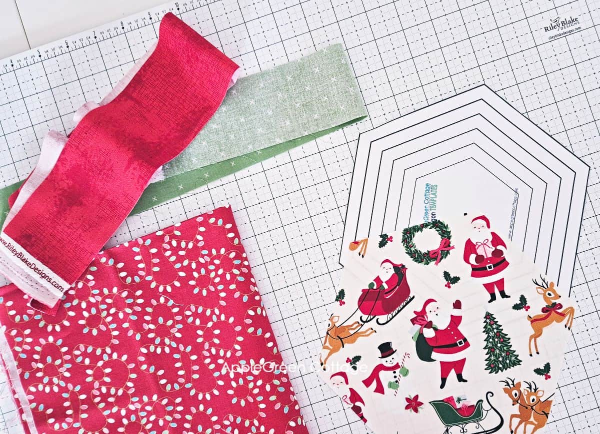 pieces of holiday themed fabric prints in red and green with a printed hexagon pattern for sewing a hexagon table topper