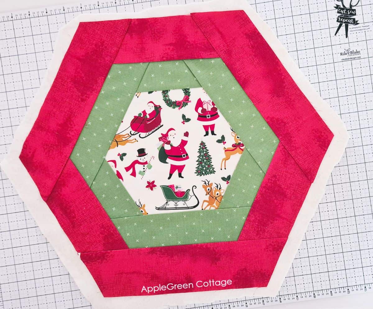 a pieced red hexagon table runner quilt placed on a cutting mat