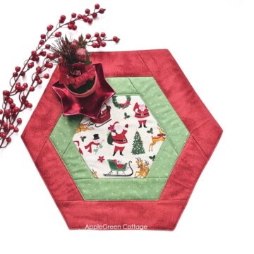 a pieced red hexagon table runner in holiday prints with a red poinsettia pot plant decoration