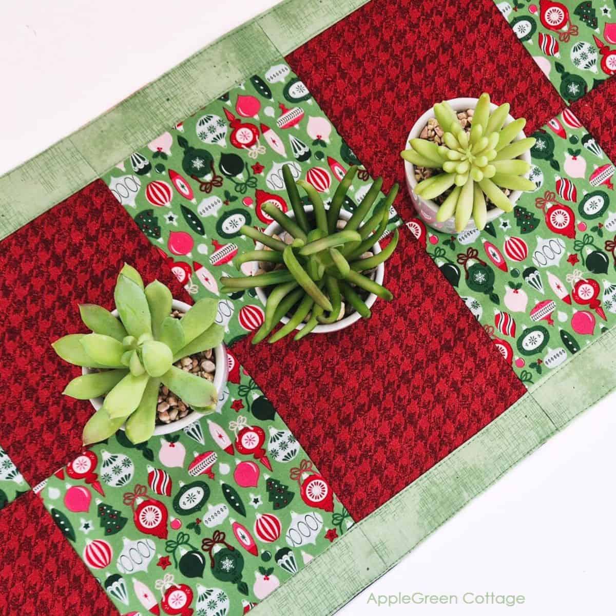 A beautiful quilted Christmas table runner featuring red and green christmas prints, with three small plant pots on it