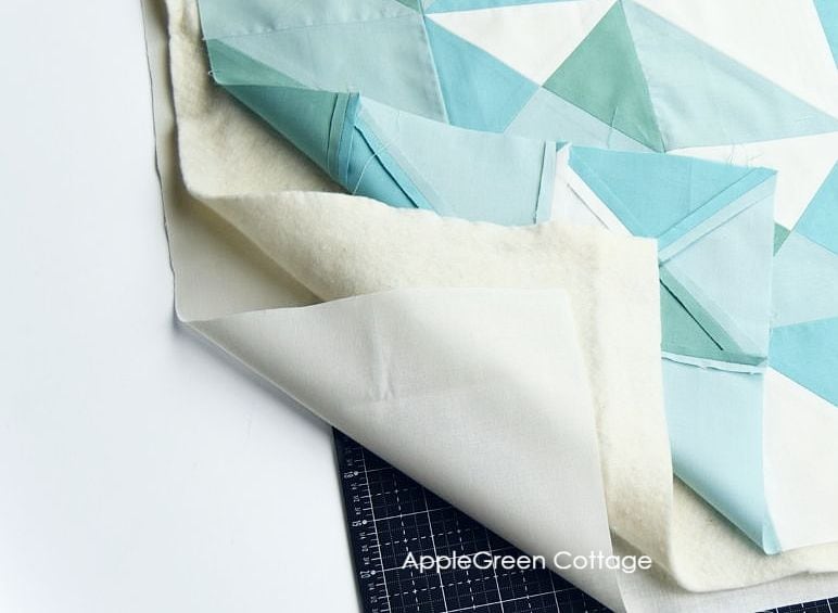 three layers of a quilt on a cutting table: blue and white pieced quilt top placed on a layer of batting and quilt backing at the bottom