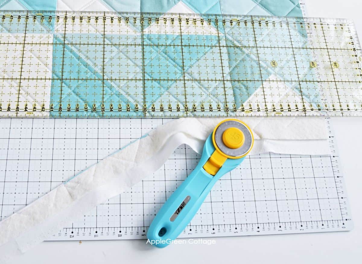 aqua rotary cutter next to a square quilting ruler placed on a semi-finished quilt ready to be squared up