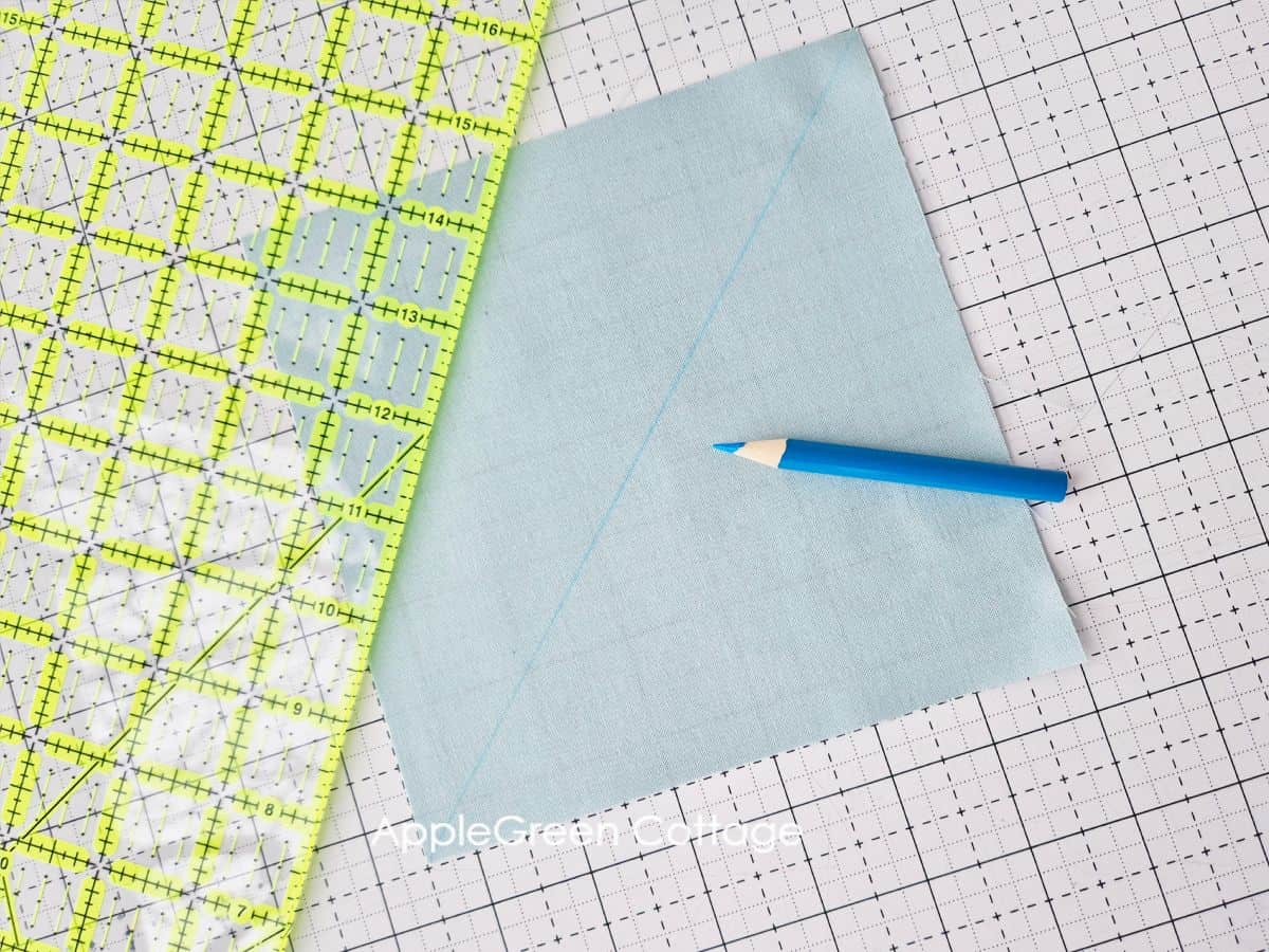 Using a ruler and pencil to mark diagonal lines on fabric for Half Square Triangles.