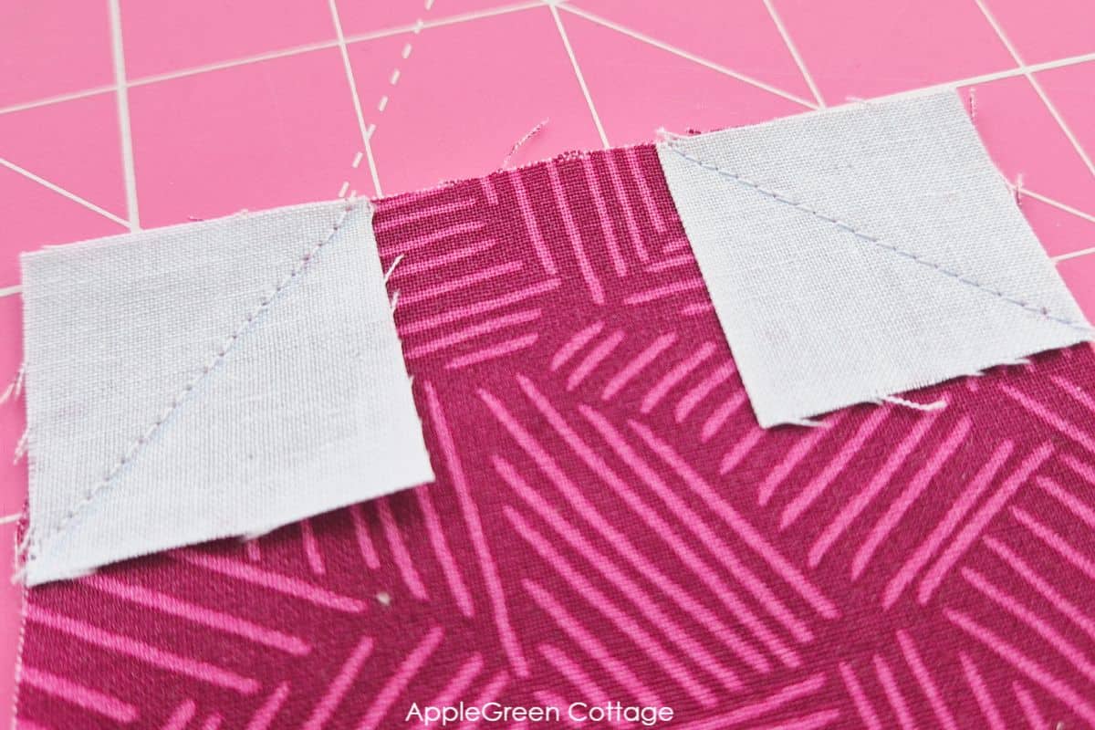Close-up of stitched white corner squares on a red heart quilt block fabric, showcasing fine sewing details.