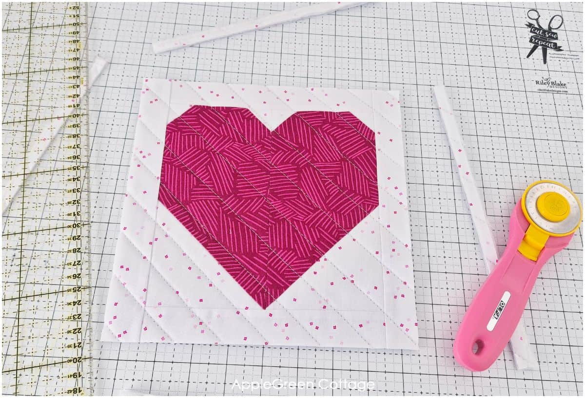 A partially sewn pink heart quilt block with white strips, demonstrating the construction process.