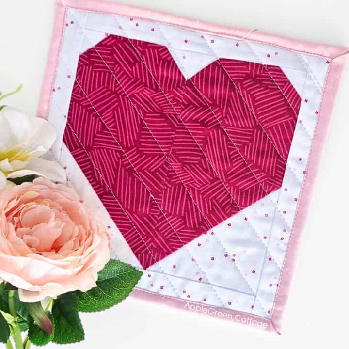 Finished heart quilt block mini quilt with soft pink binding and floral accents. A beginner-friendly quilting project perfect for gifts or home decor.
