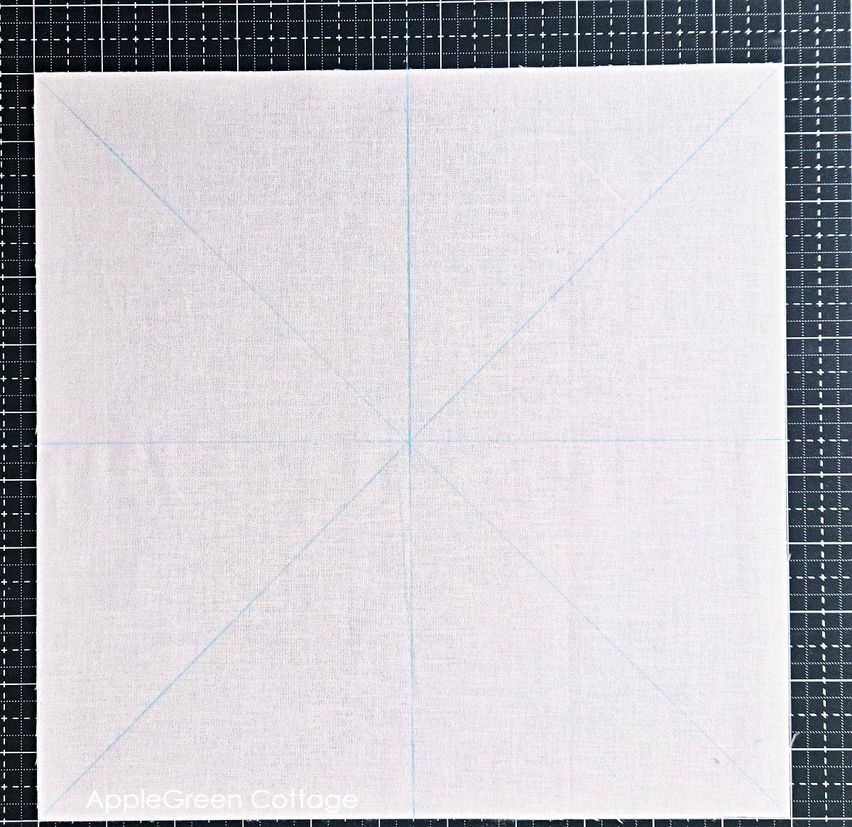White fabric square marked with diagonal and center guidelines for the Magic 8 HST method.