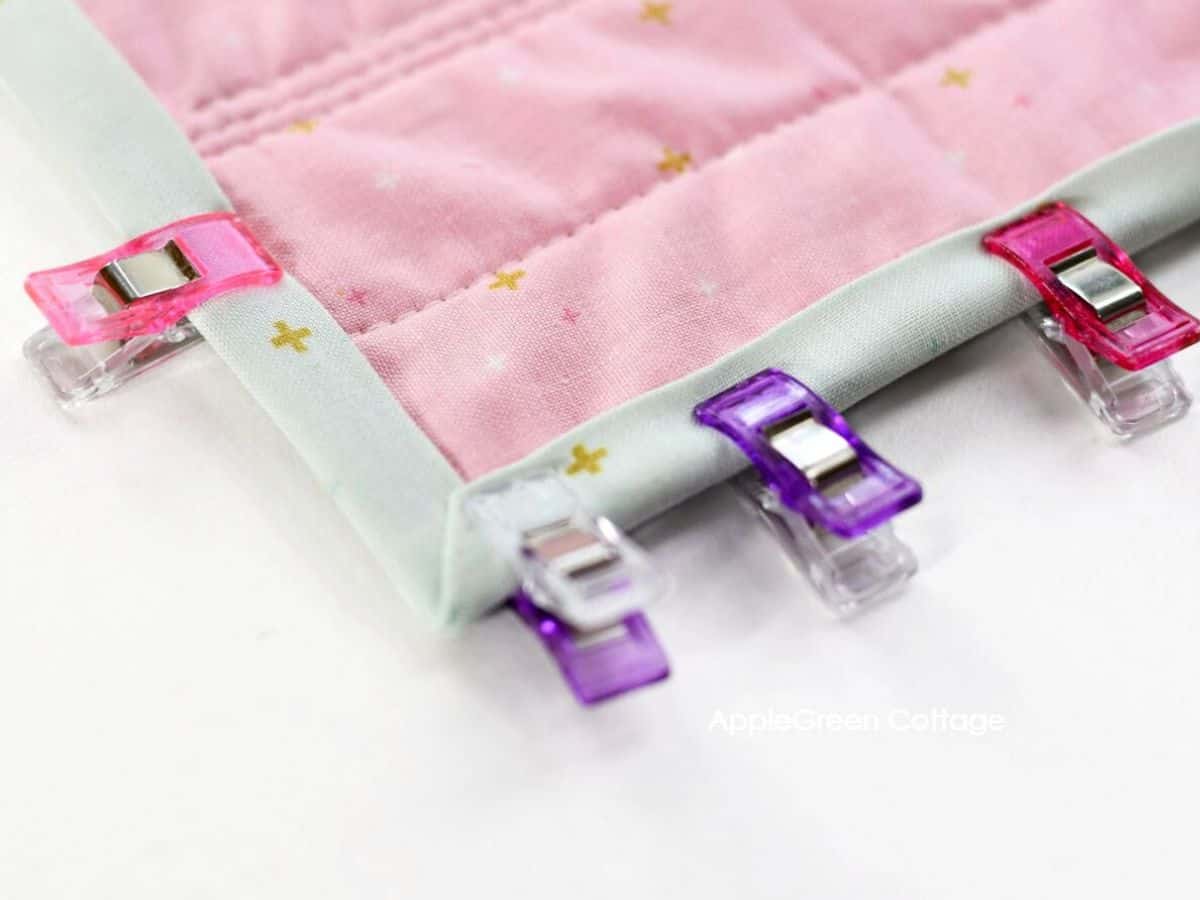 Sewing clips holding a strip of mint colored quilt binding on the corner of a quilt.