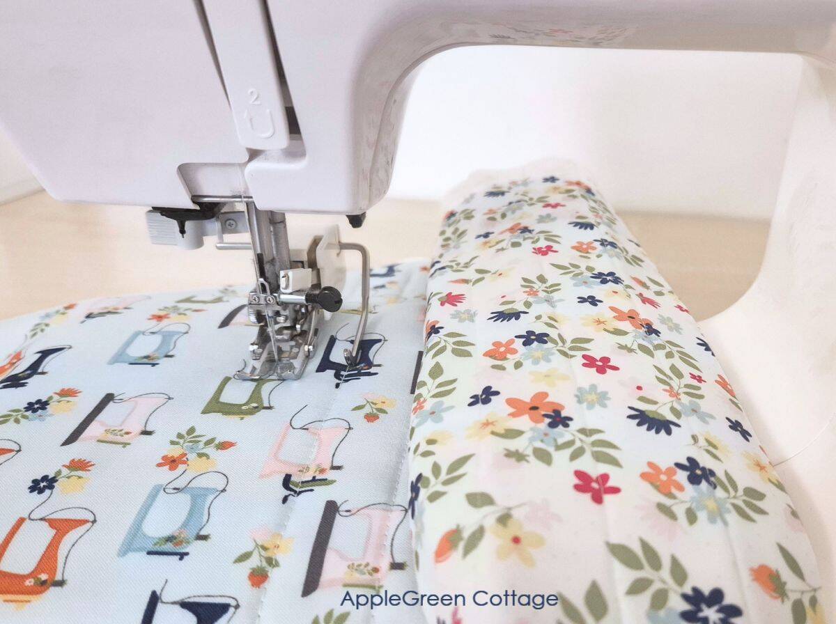 a floral fabric quilt top with layers of batting and backing being quilted on a home sewing machine