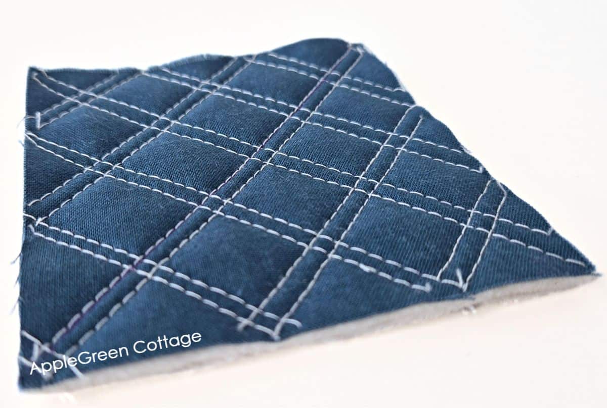 Dark blue quilted fabric with a diagonal grid pattern of white stitches, creating a textured effect.