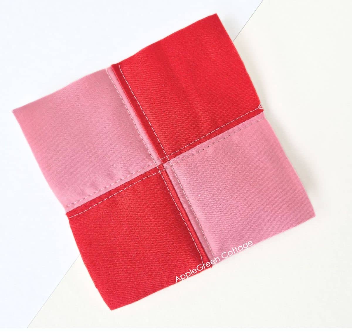 Red and pink four-patch quilt block with simple straight-line quilting stitches.
