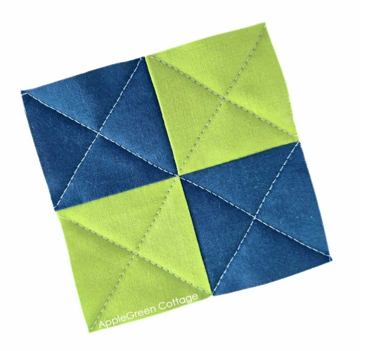 Green and navy half-square triangle quilt block with diagonal quilting stitches.