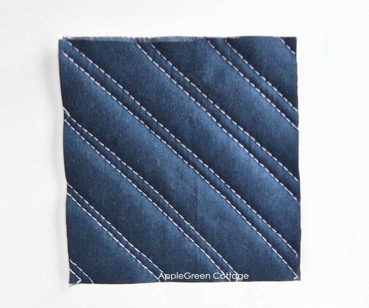 Dark blue quilted fabric with double diagonal straight-line quilting stitches.