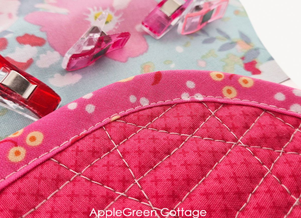 A finished pink, straight-line quilted potholder in a curved design.