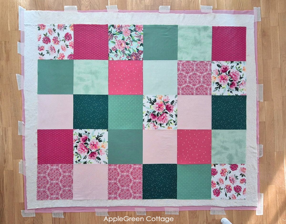 Layering quilt backing, batting and quilt top on the wooden floor to be basted.