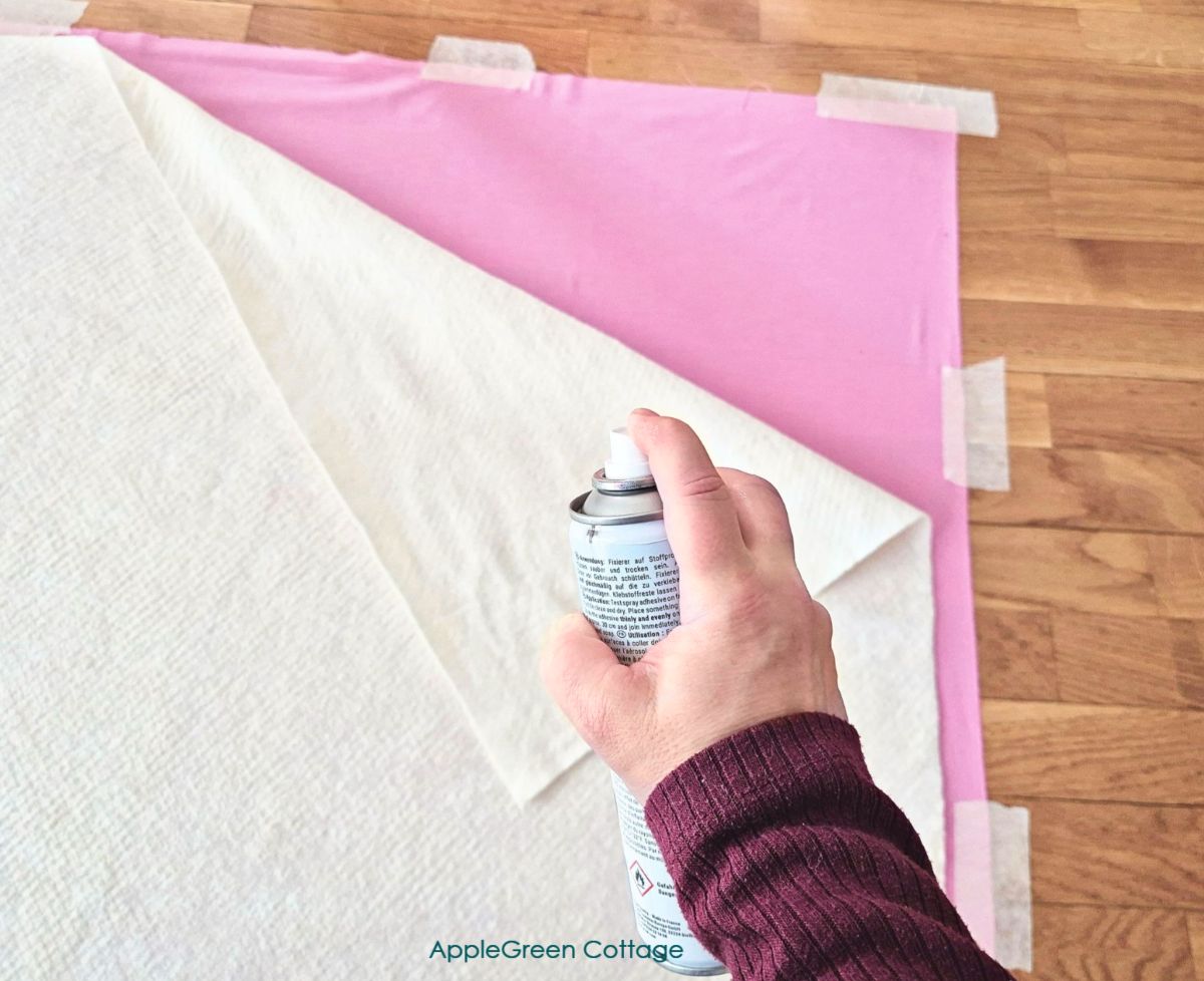 a hand holding a temporary basting spray and spray basting quilt batting to the backing.
