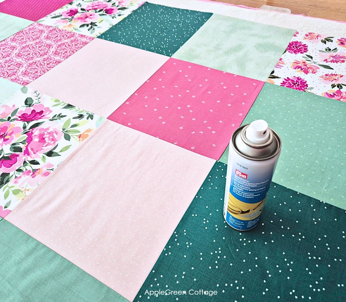 Spray basting a colorful patchwork quilt top laid flat on batting and backing fabric.