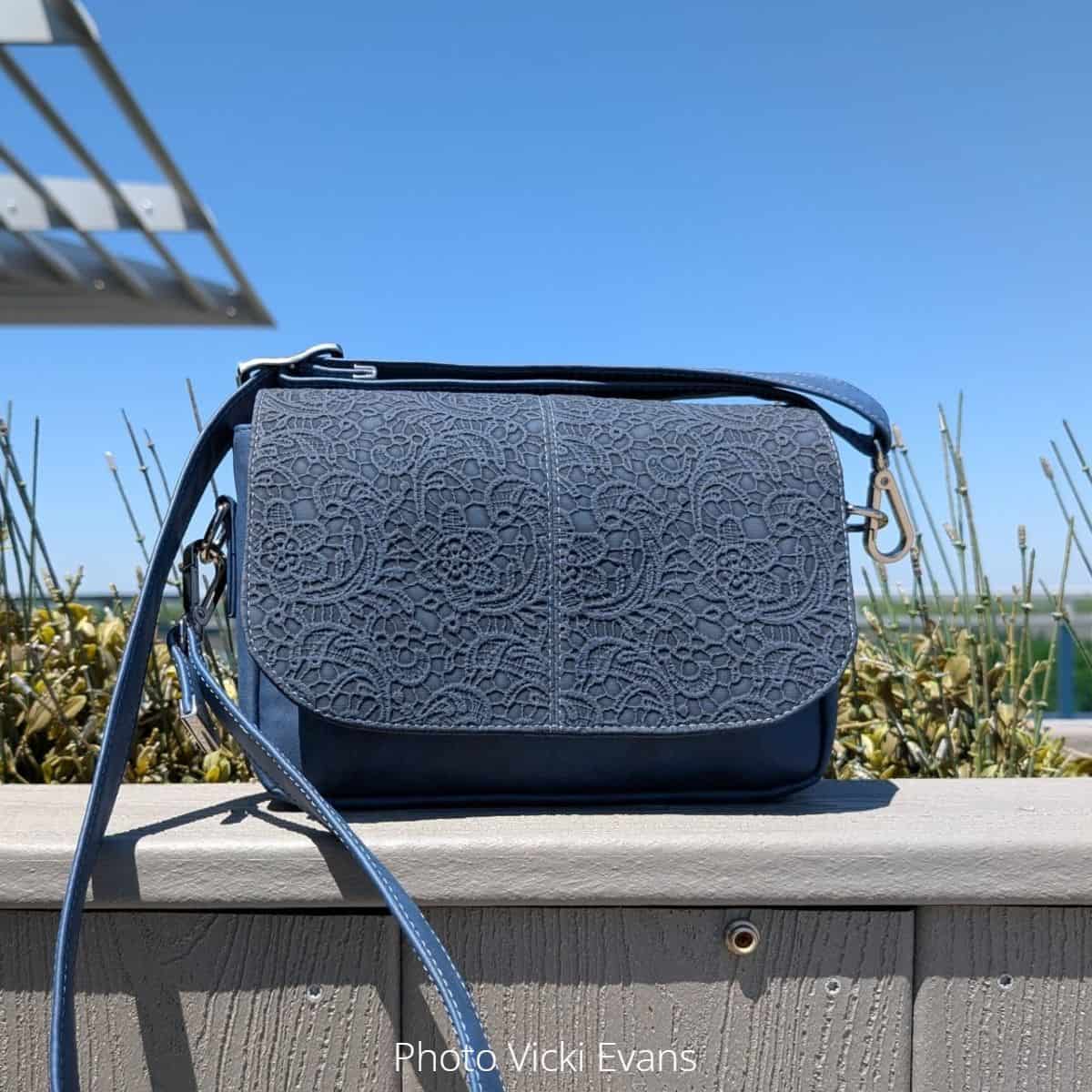 Monochrome blue textured vinyl purse with flap closure, adjustable strap, and clean topstitching.
