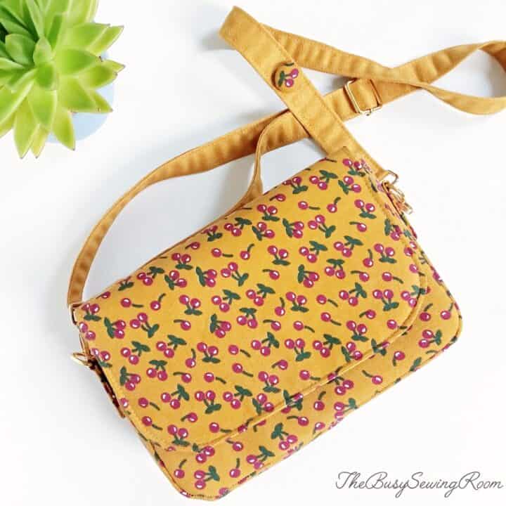 A finished handmade purse with a flap, sewn with cheryy print on corduroy fabric and a handmade microsuede strap.
