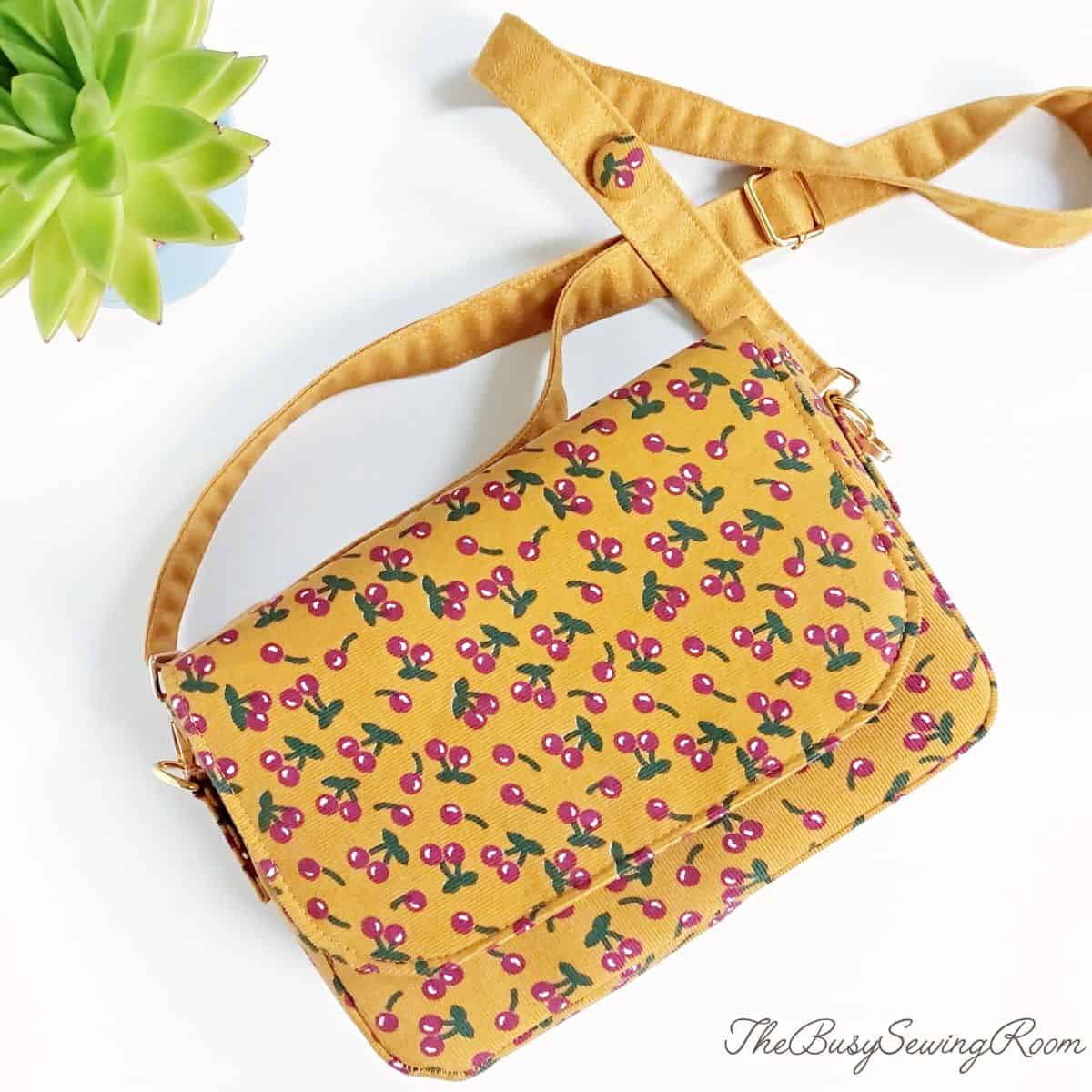 A finished handmade purse with a flap, sewn with cheryy print on corduroy fabric and a handmade microsuede strap.