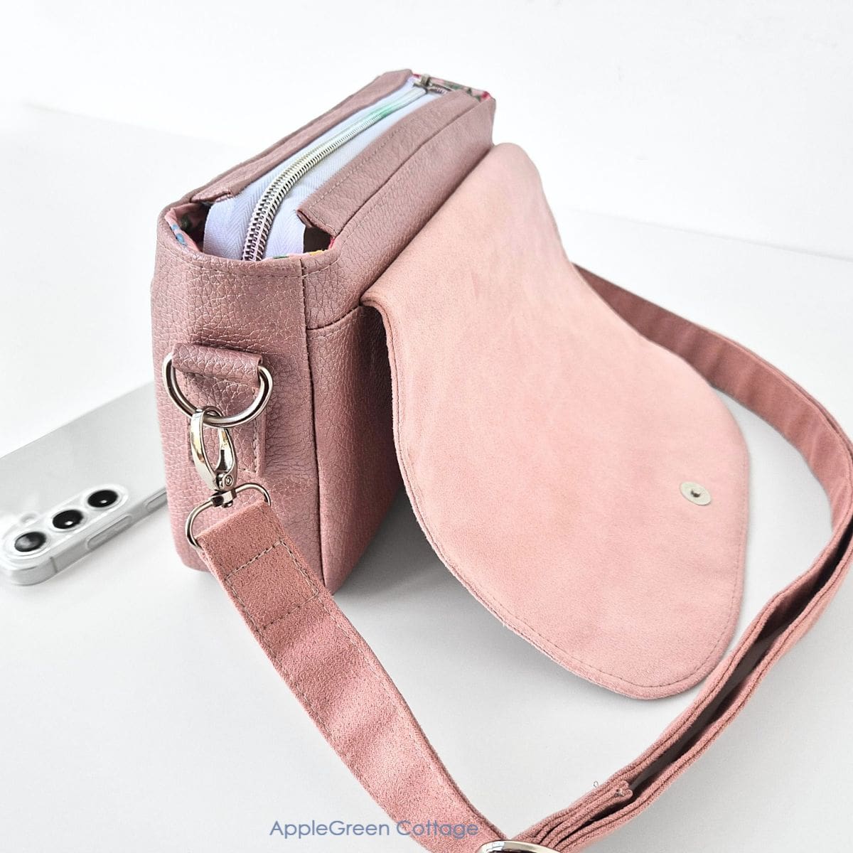 Pink faux leather crossbody bag with an open flap and showing the side strap connector, small bag made using the Elarina purse sewing pattern.