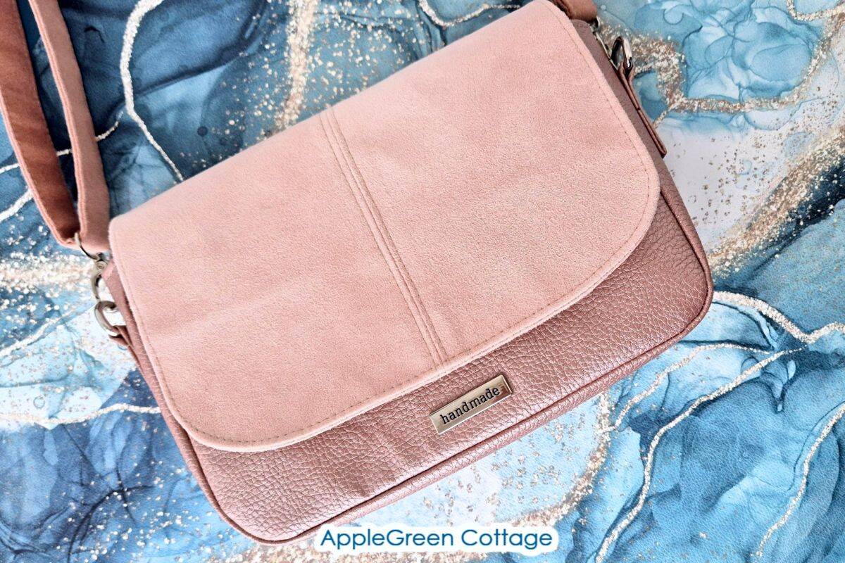 Pink faux suede and leather crossbody purse shown on blue fabric background, made with the Elarina bag pattern.
