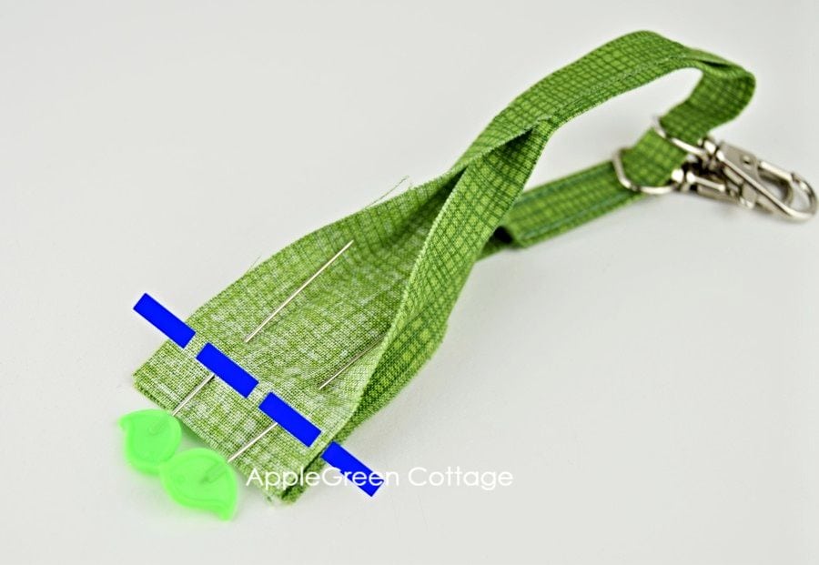 Folded green fabric strip, ready for sewing into a keyholder strap and two swivel hooks on it.