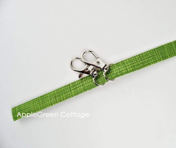 Folded green fabric strip, cut for a keyholder strap and two swivel hooks on it.