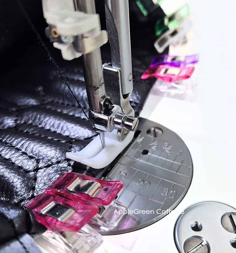 Janome Hd9 needleplate closeup showing Janome's ultra glide machine foot sewing over several layers of black vinyl, clipped together using wonder clips.