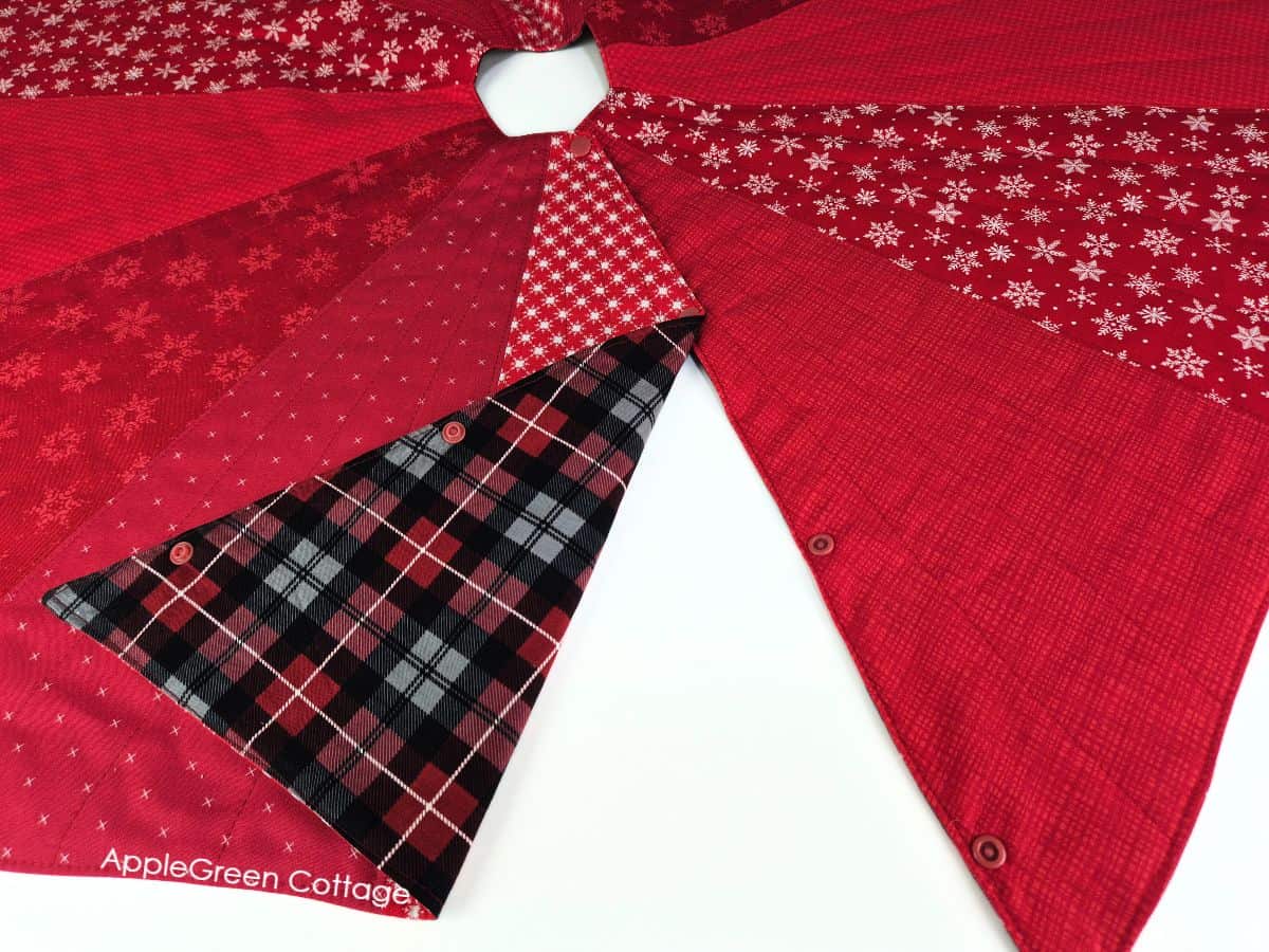 Reversible quilted Christmas tree skirt with red and plaid fabrics and snap closure detail.